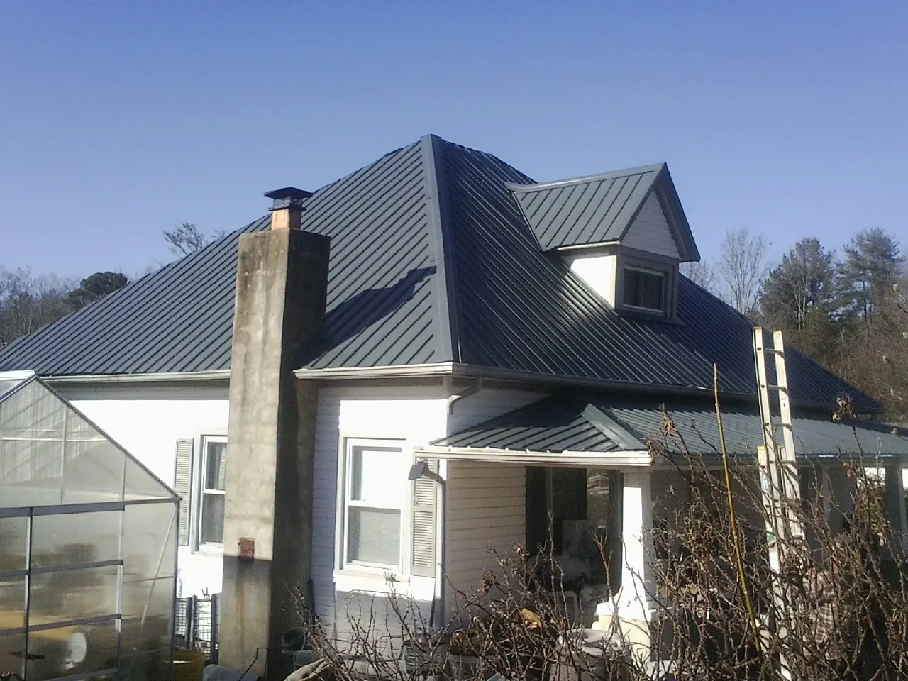 Dark blue standing seam metal roof on a white farmhouse with dormer — Slate & Tile Roof Repair by Roofing Brothers in Elkview