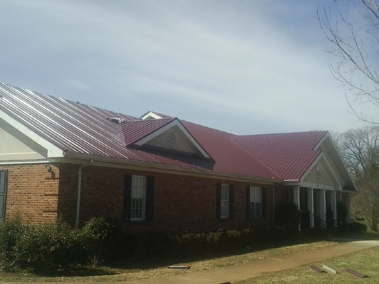 Red metal roof with gabled entries on a long brick building, from a Hail Damage Roof Repair job in Elkview
