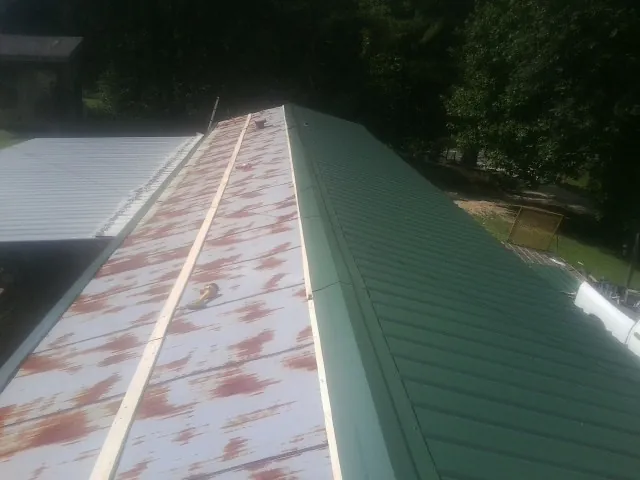 Old rusted panels beside newly installed green metal roofing — Wind Damage Roof Repair by Roofing Brothers in Elkview