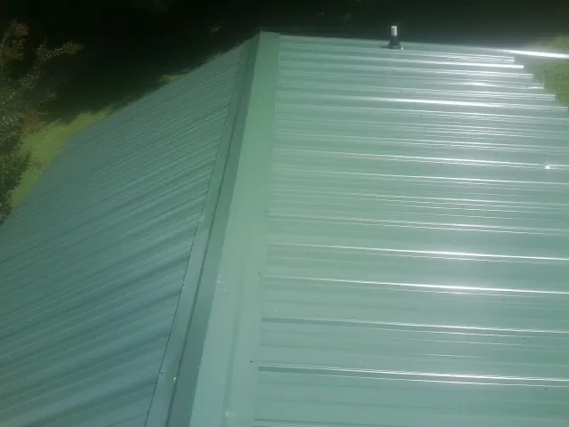 New green metal panels meeting at the ridge of a roof — Flat Roof Repair work by our crew in Elkview