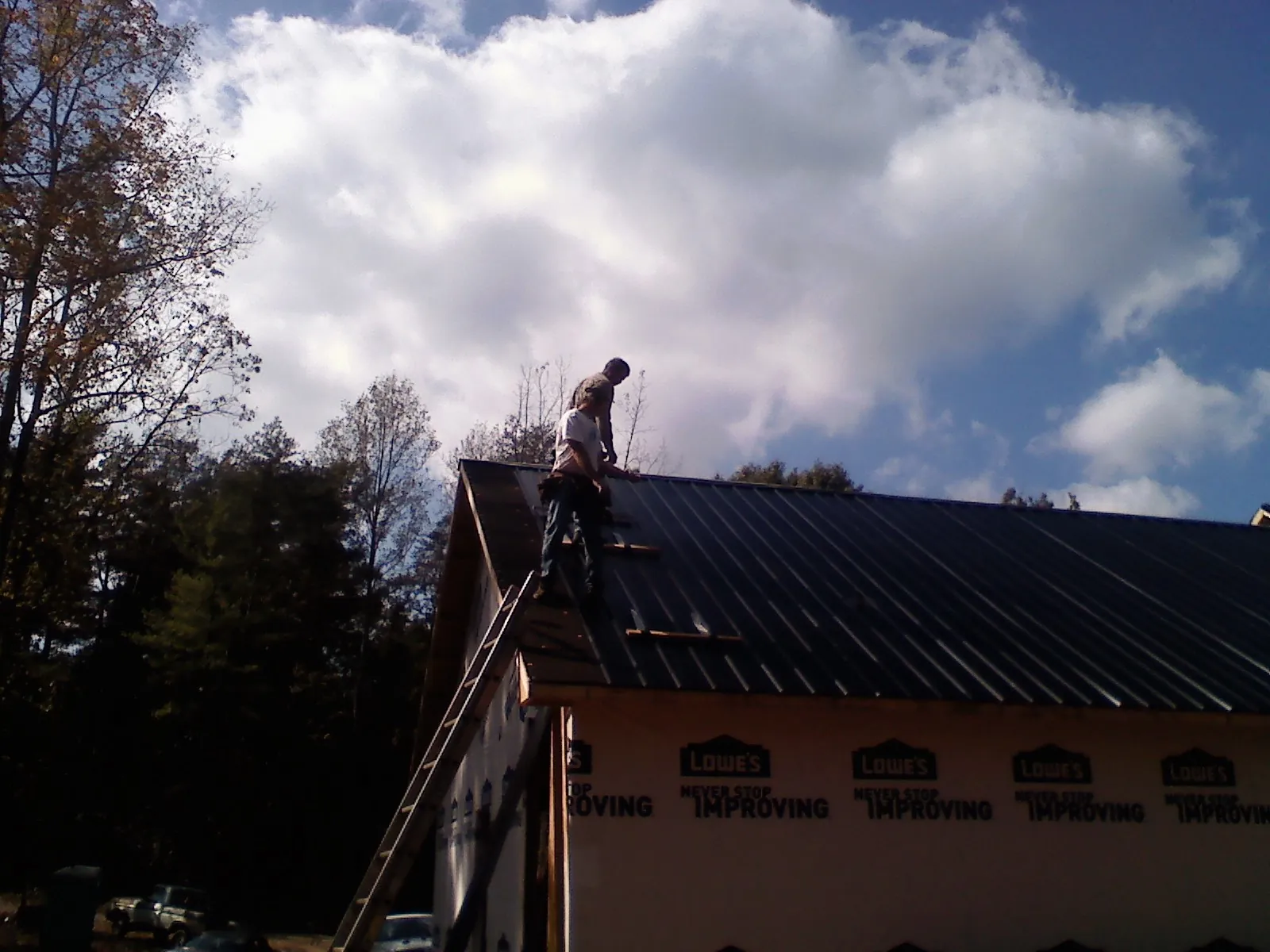 Roofer fastening dark metal panels high against a cloudy sky, from a Roof Inspection job in Elkview