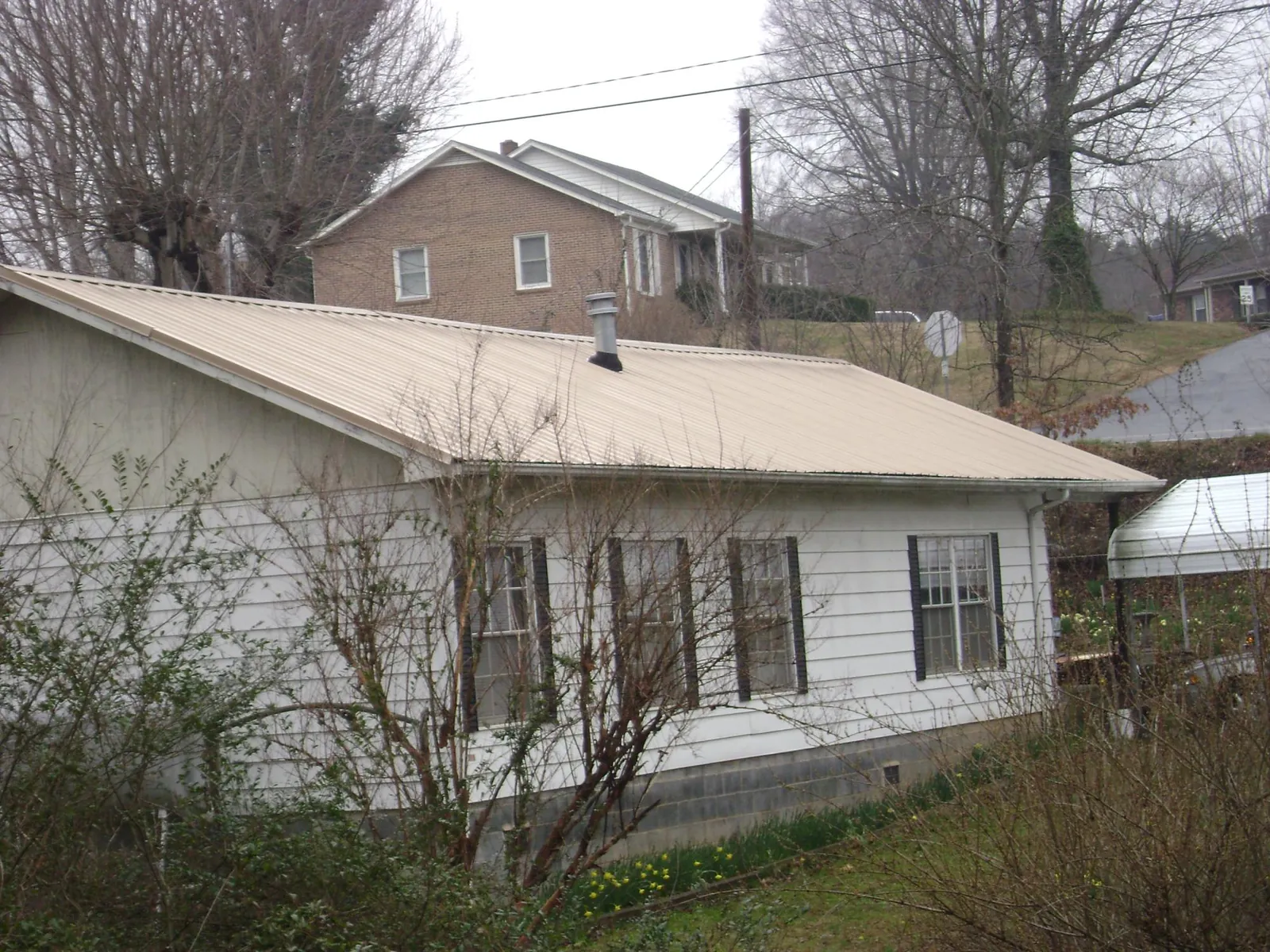 Tan metal roof on a white sided house set into a hillside — Commercial Roofing by Roofing Brothers in Elkview